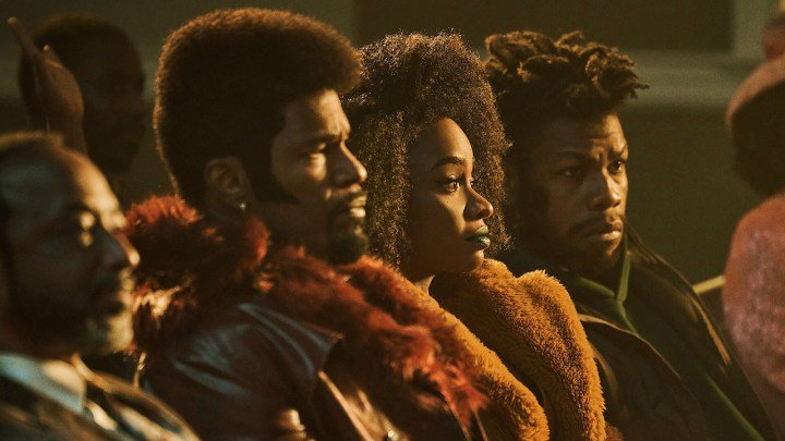 Dos hombres y una mujer sentados juntos en una especie de teatro en una escena de They Cloned Tyrone en Netflix.