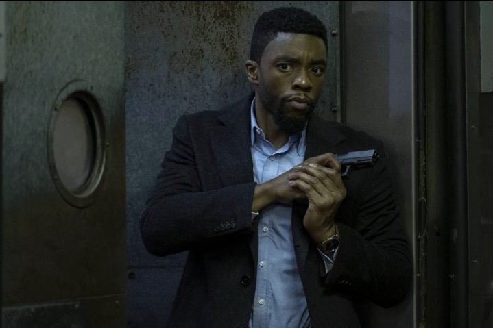 Chadwick Boseman sostiene una pistola y se para contra una pared.