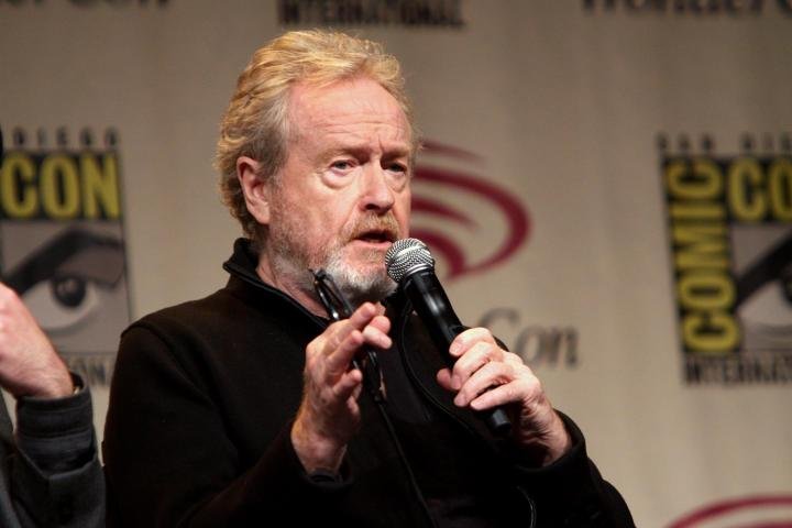 Ridley Scott sostiene un micrófono y habla.