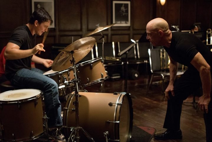 Miles Teller toca la batería mientras JK Simmons mira al frente en Whiplash.