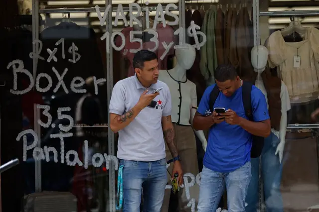 Personas frente a una tienda que exhibe precios en bolívares (moneda oficial venezolana) y dólares estadounidenses en Caracas, Venezuela, el 2 de junio de 2025.