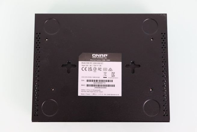 Zona inferior del switch QNAP QSW-3205-5T con las marcas para los tacos de goma y agujeros de pared