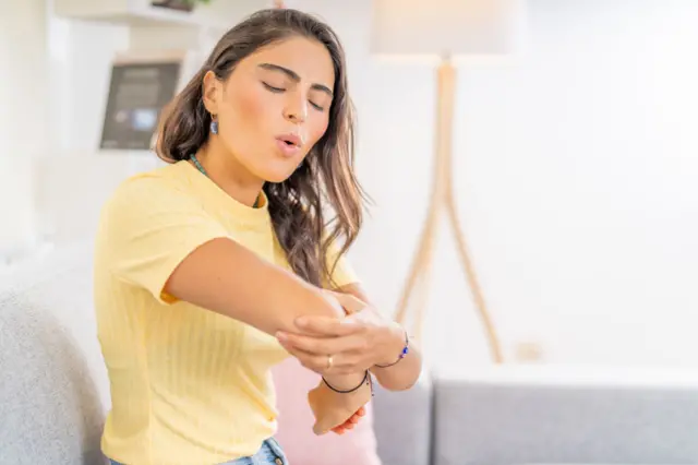 Una mujer se mira el codo con dolor