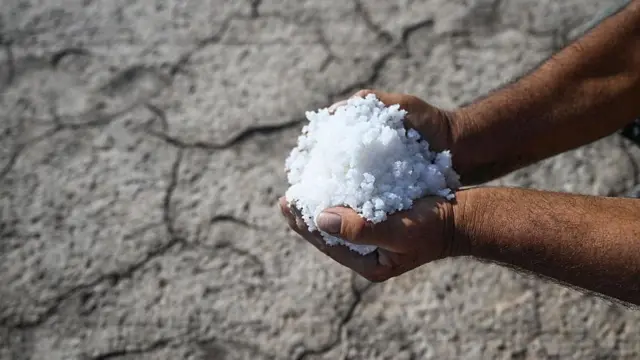 Un hombre sostiene sal muy blanca con sus manos mientras al fondo se ve un terreno agrietado por la sequedad. 