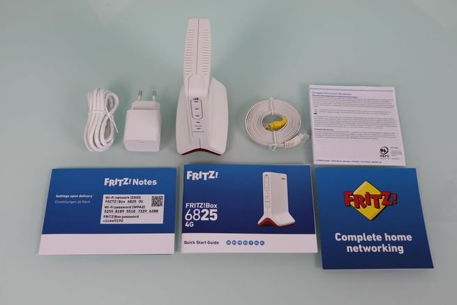 Router FRITZ!Box 6825 4G con accesorios: fuente de alimentación, cables y manuales de instrucciones.