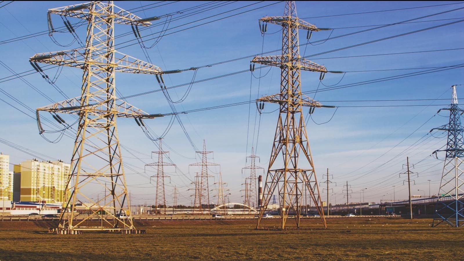 Líneas de alta tensión y torres de electricidad metálicas en un entorno urbano bajo un cielo despejado.