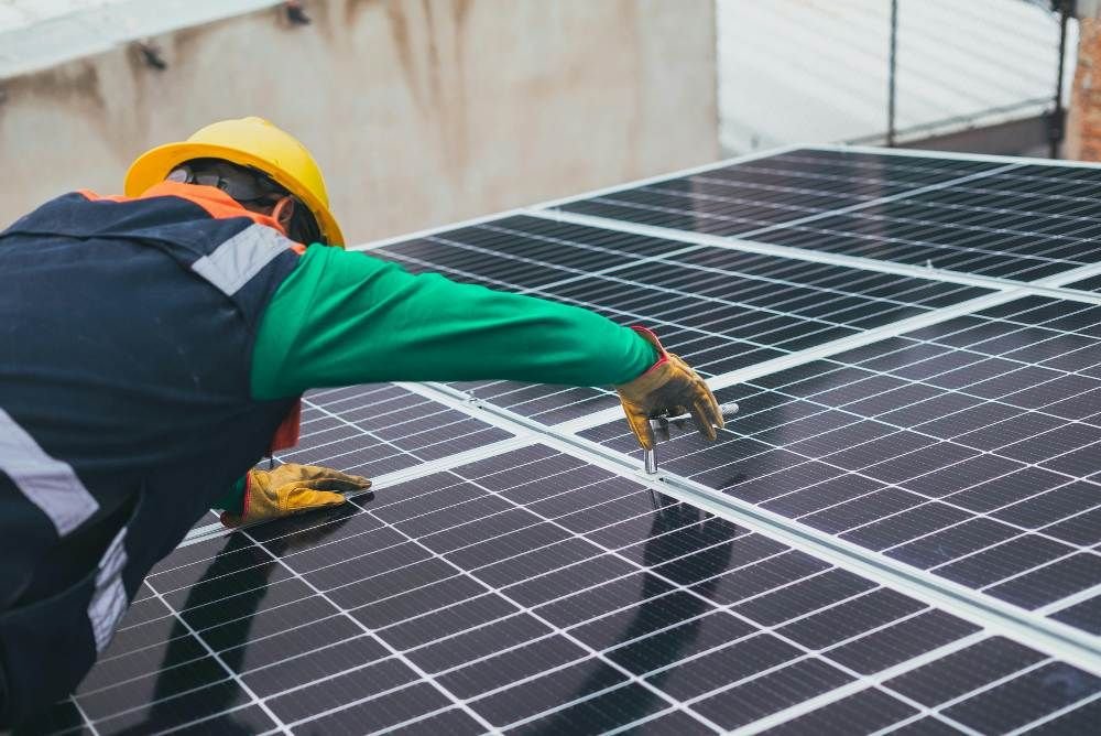 Técnico instalando paneles solares fotovoltaicos en un tejado utilizando herramientas manuales.